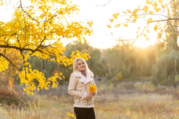 Buitenmodefoto van jonge mooie dame omringd door herfstbladeren