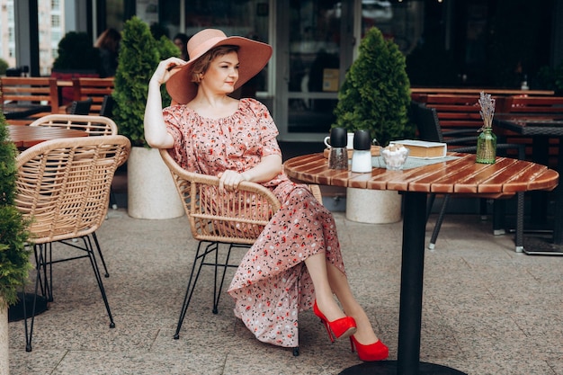 Buitenmodeportret van een prachtige vrouw die in een café zit Ik drink koffie en lees een oud boek een vrouw in een jurk en een hoed