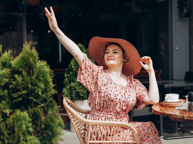 Buitenmodeportret van een prachtige vrouw die in een café zit Ik drink koffie en lees een oud boek een vrouw in een jurk en een hoed