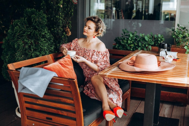 Buitenmodeportret van een prachtige vrouw die in een café zit Ik drink koffie en lees een oud boek een vrouw in een jurk en een hoed