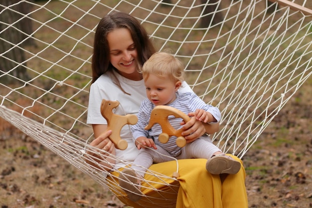 Buitenopname van een speelse familie ontspannen in het bos moeder en kind zitten in een hangmat en spelen met houten speelgoed tijdens het weekend in de open lucht