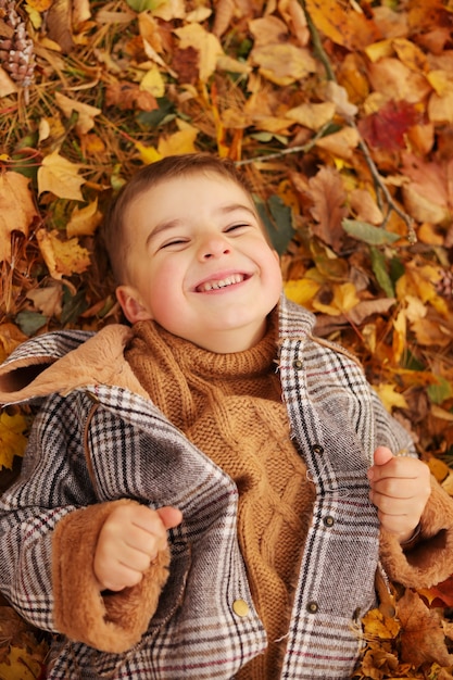 Buitenplezier in de herfst. kind spelen met herfst gevallen bladeren in park. gelukkig jongetje liggend op gele bladeren buitenshuis. uitzicht van boven.