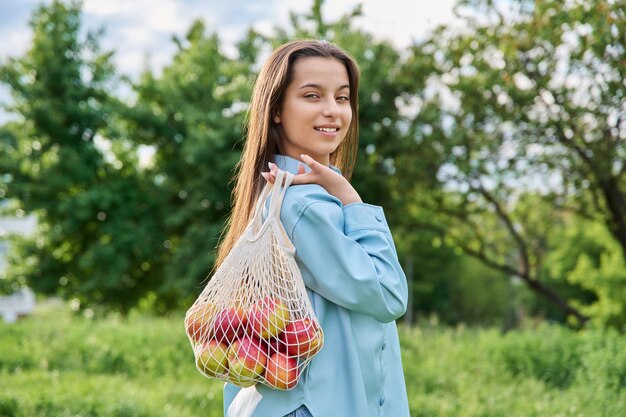 Buitenportret van een mooi tienermeisje met een netzak appels