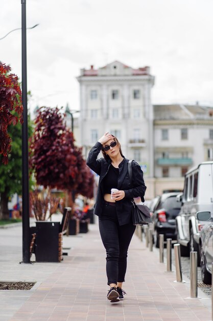 Buitenshuis lifestyle portret van prachtige brunette meisje. Koffie drinken en wandelen door de stadsstraat.