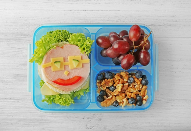 Foto buitensporige sandwichdruif en noten in lunchbox op lichte houten achtergrond