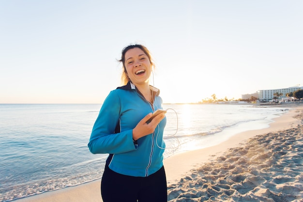 Buitensport, fitnessgadget en mensenconcept - Glimlachende vrouwelijke fitness met smartphone met oortelefoons.