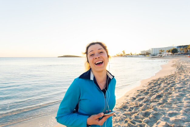 Buitensport, fitnessgadget en mensenconcept - Glimlachende vrouwelijke fitness met smartphone met oortelefoons.