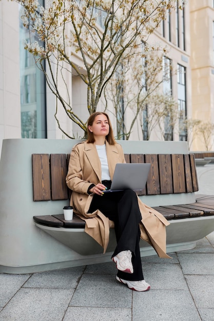 Buitenwerkruimte Een freelancer werkt aan een laptop op een bankje tegen de achtergrond van een kantoorgebouw