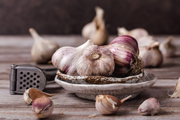 The bulbs of garlic, slice, on ceramic plate on a wooden table, the garlic press