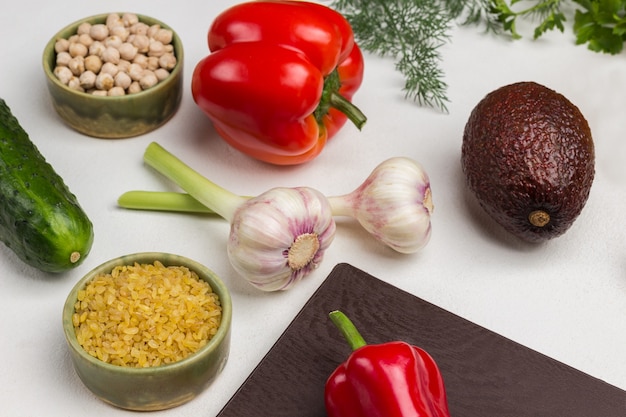 Bulgur and chickpeas in bowls. Garlic, pepper and avocado on table. White background.