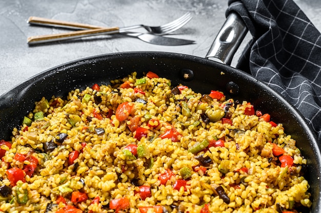 Bulgur gekookt met groenten en kippenvlees in een pan. Grijze achtergrond.