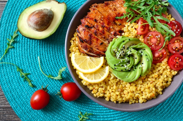 Bulgur met gegrilde kipfilet, verse groenten, avocado, rucola. Dieet lunch op een houten tafel. Gezond eten. Bovenaanzicht.