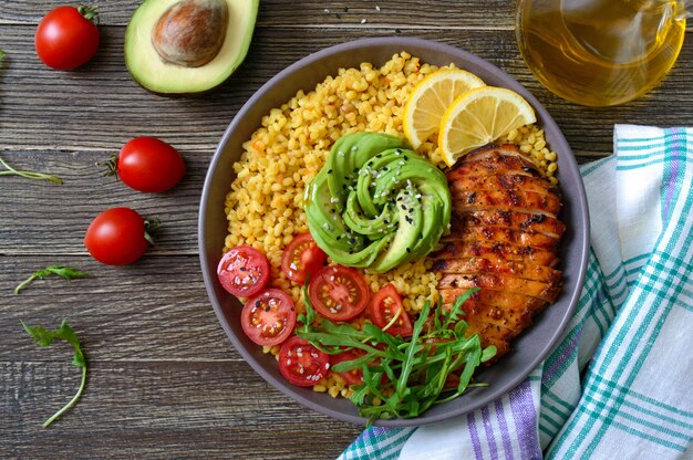 Bulgur met gegrilde kipfilet, verse groenten, avocado, rucola. Dieet lunch op een houten tafel. Gezond eten. Bovenaanzicht.