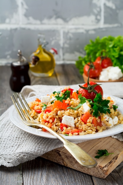 Bulgur met geroosterde paprika, tomaten, peterselie en fetakaas op een houten achtergrond. Selectieve aandacht.