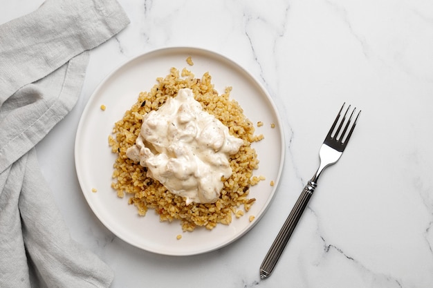 Bulgur met kip en roomsaus. Dineridee met bulgur pap en kipfilet. Witte achtergrond en witte plaat. Bovenaanzicht.