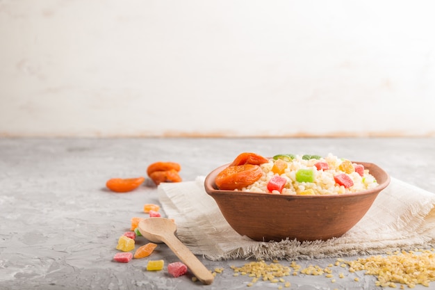 Porridge di bulgur con albicocche secche e frutta candita in ciotola di argilla su una superficie di cemento grigio e tessuto di lino. vista laterale, messa a fuoco selettiva, copia spazio.