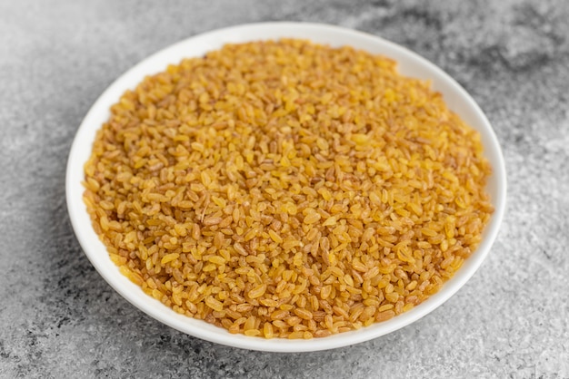 Bulgur in a white saucer on a gray concrete background