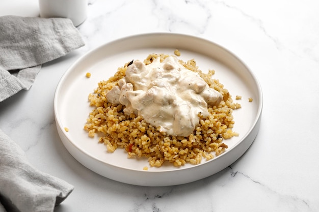 Bulgur with chicken and cream sauce. Dinner idea with bulgur porridge and chicken fillet. White background and white plate