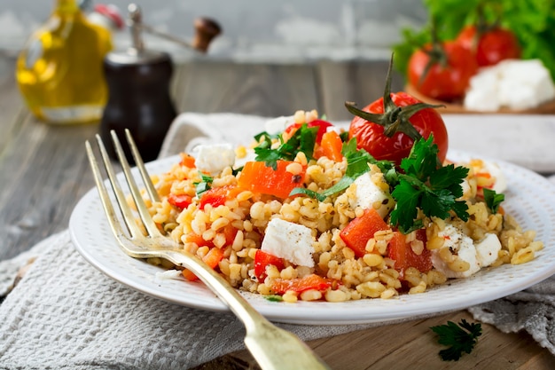 Bulgur with roasted peppers, tomatoes, parsley and feta cheese on a wooden background. Selective focus.