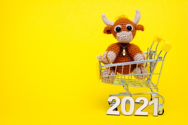 The bull is the symbol of the new year 2021. knitted toy bull in a supermarket toy cart