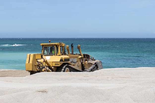 Bulldozer bezig met het verspreiden van zand op een strand en zee op de achtergrond