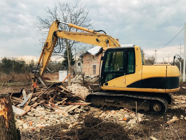 Bulldozer clearing land from old bricks and concrete from walls\
with dirt and trash backhoe machinery ruining house excavator\
destroying brick house on land in countryside