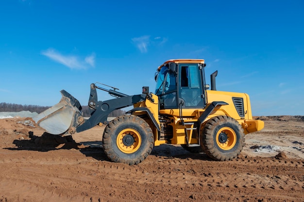 Bulldozer o caricatore sposta la terra in cantiere contro il cielo blu una macchina movimento terra sta livellando il sito costruzione di attrezzature pesanti per lavori di sterro