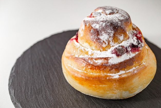 Bun curled with cherries and sprinkled with powdered sugar on slate stone plate round side view selective focus