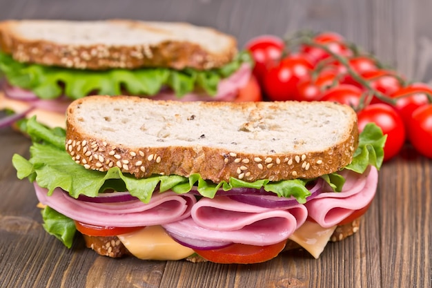 Bun and sandwiches with ham cheese and tomato on a wooden board