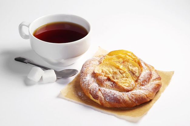 Bun with apples and cup of tea for breakfast on white