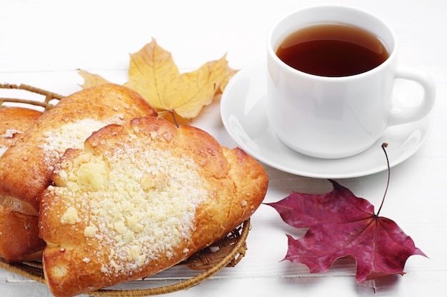 Bun with cup of tea and maple leaves on white table