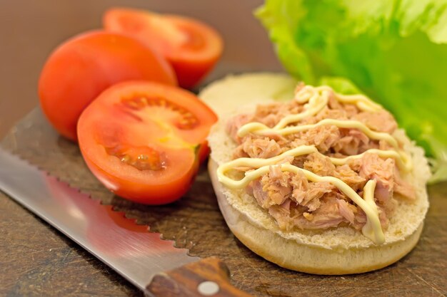 Bun with tuna tomatoes and lettuce on a cutting board