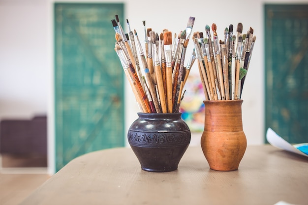 A bunch of art brushes standing in ceramic vases, on the table in the art studio.