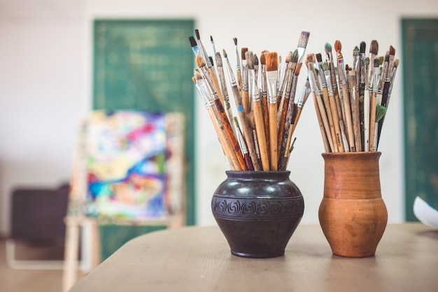 A bunch of art brushes standing in ceramic vases, on the table in the art studio.