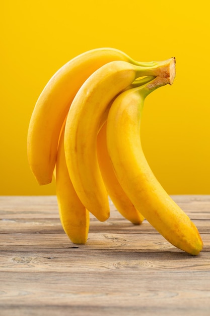 Bunch of bananas on wooden table on yellow background