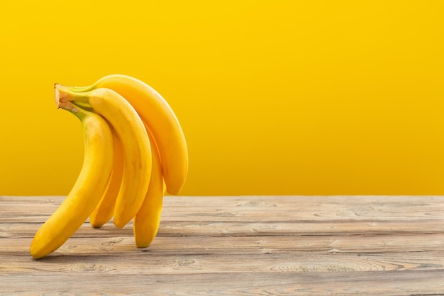 Bunch of bananas on wooden table on yellow background