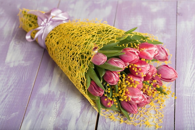 Bunch of beautiful pink tulips and mimosa flowers on a purple wooden surface. Closeup