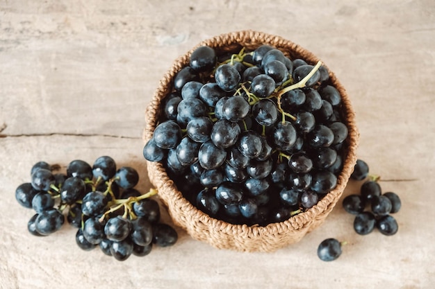 Bunch of black grapes in a round wicker basket on a old wooden table