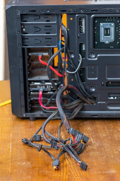 Bunch of computer power supply wires sticking out from opened black pc case closeup with selective focus