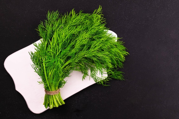 A bunch of dill on a white wooden board on a black background Copy space