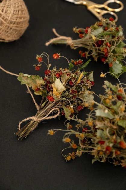 Bunch of dried wild strawberry twigs with berries on dark table surface Herbal medicine remedy