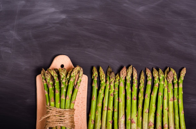 A bunch of fresh asparagus on a cutting board and stems on a black chalk board with place for text. Seasonal spring harvest. Flat lay, copy space. Healthy food concept. View from above. Close-up