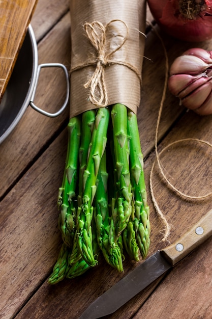 Mazzo di asparagi freschi legati con spago, utensili da cucina coltello all'aglio sul tavolo di legno