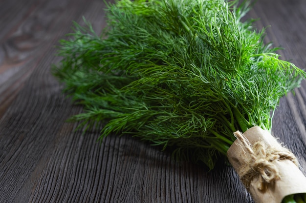 Bunch of fresh dill and spices on dark wooden table.