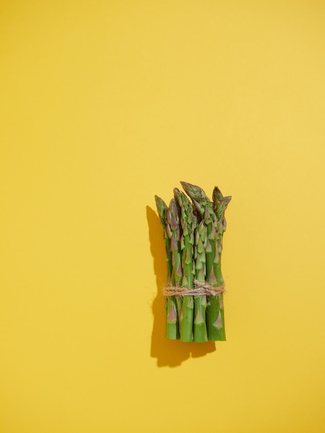 Bunch of fresh green asparagus heads tied with string Top view on yellow background Bright illumination with shadows