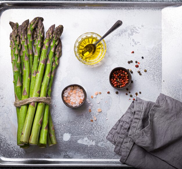 Bunch of fresh green organic asparagus ready for cooking on baking tray with olive oil and seasonings, top view, close up. Asparagus for clean and healthy diet and eating