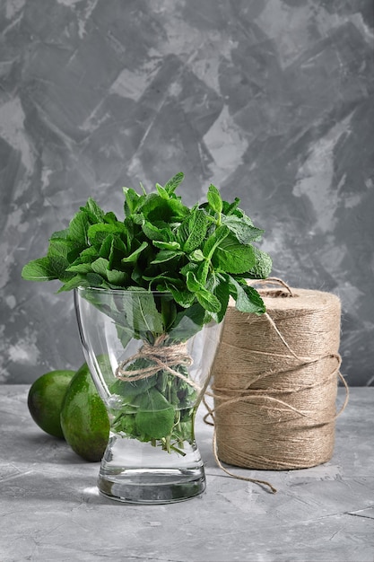 灰色の背景に水の花瓶に新鮮なミントの束。生鮮食品、包装、製品のオンライン配達の概念。スペースのコピー。