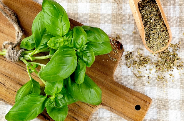 Bunch of fresh organic basil in cutting board and dry basil on wooden spoon on the rustic background