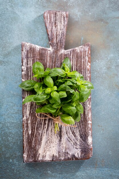 Bunch of fresh organic basil in cutting board on rustic wooden background