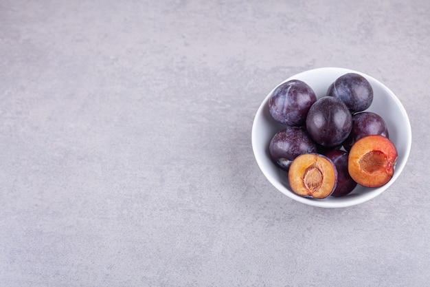 Bunch of fresh purple plums placed in white bowl.